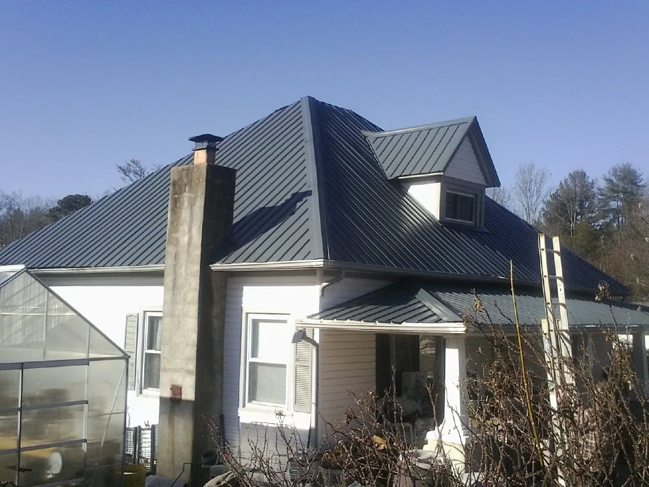 Dark blue standing seam metal roof on a white farmhouse with dormer — Slate & Tile Roof Repair by Roofing Brothers in Dix