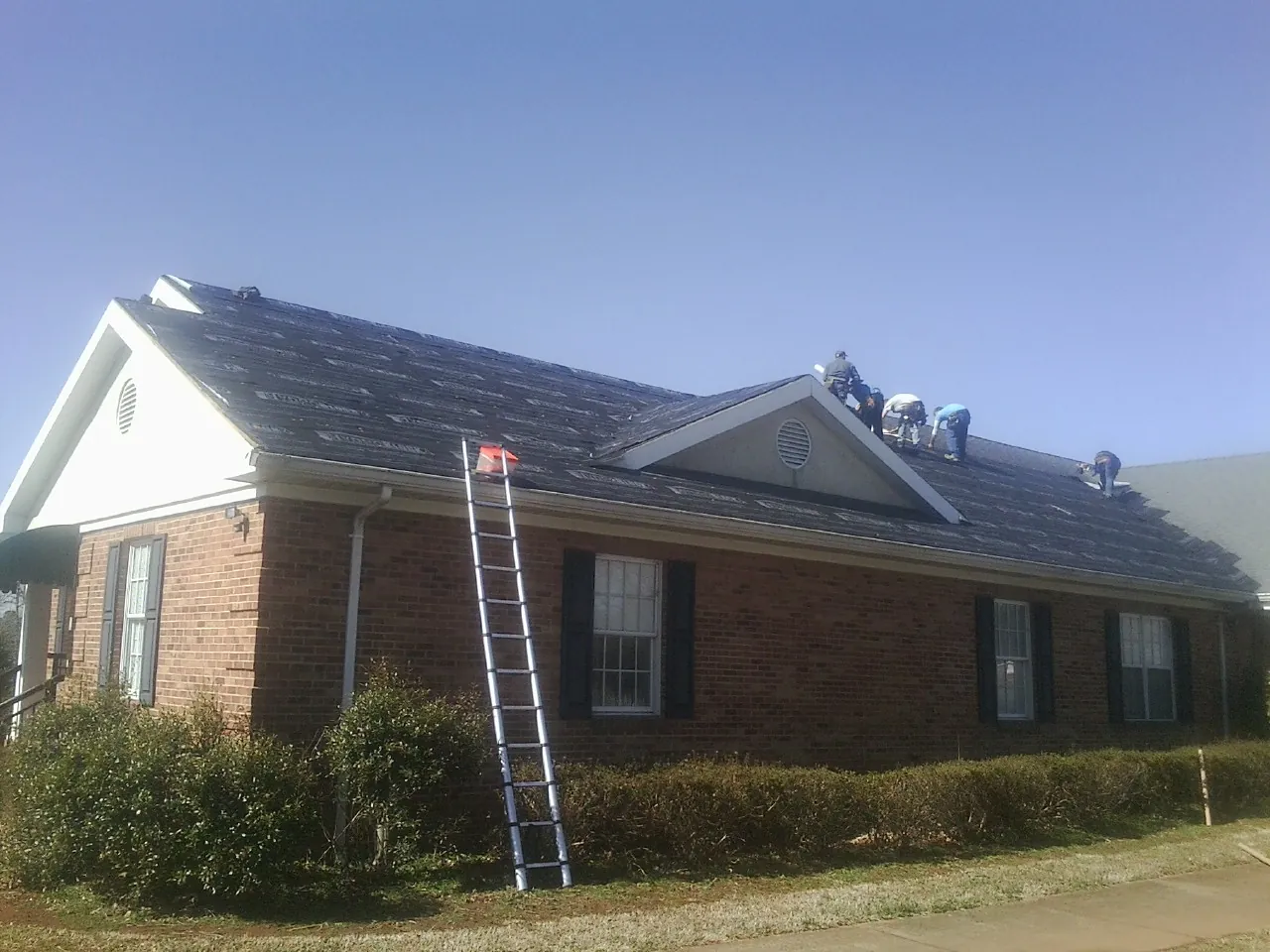 Crew tearing shingles off a brick ranch roof with a ladder set — Emergency Roof Repair work by our crew in Dix