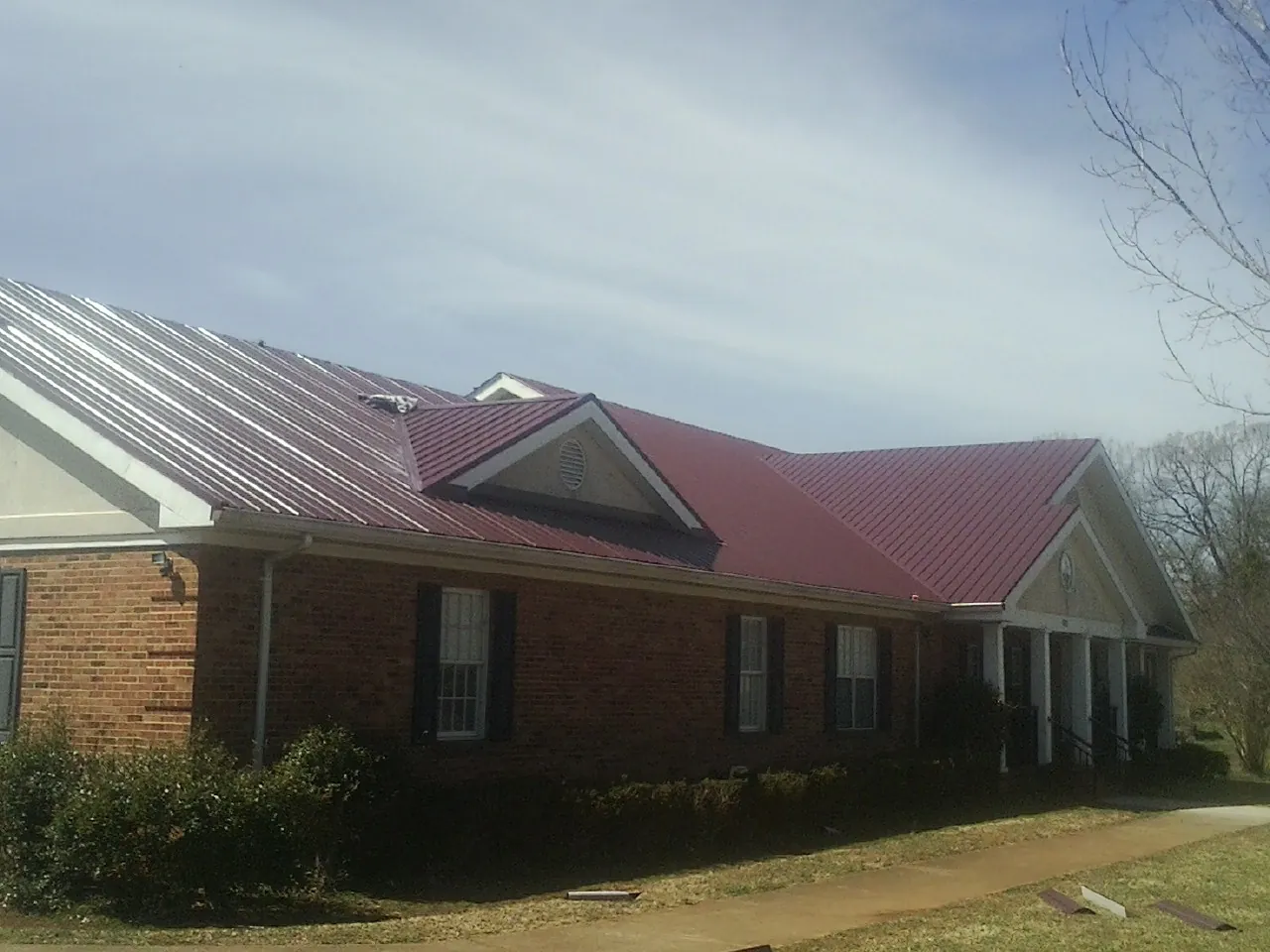 Red metal roof with gabled entries on a long brick building, from a Hail Damage Roof Repair job in Dix