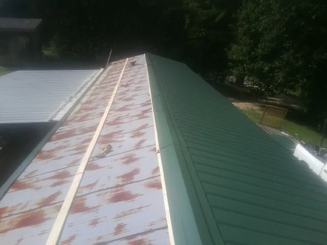 Old rusted panels beside newly installed green metal roofing — Wind Damage Roof Repair by Roofing Brothers in Dix
