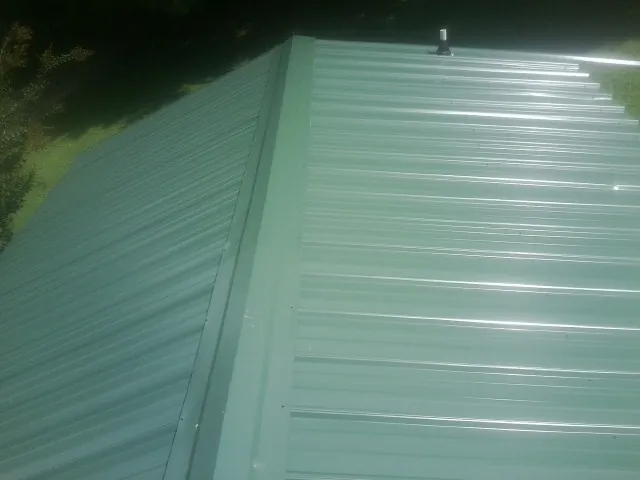 New green metal panels meeting at the ridge of a roof — Flat Roof Repair work by our crew in Dix
