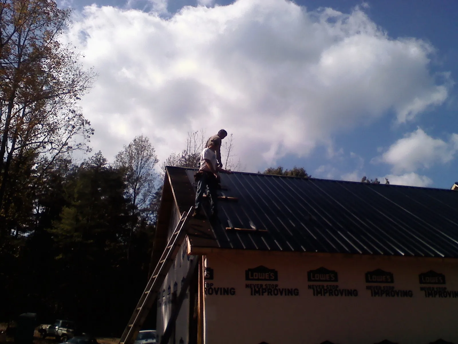 Roofer fastening dark metal panels high against a cloudy sky, from a Roof Inspection job in Dix