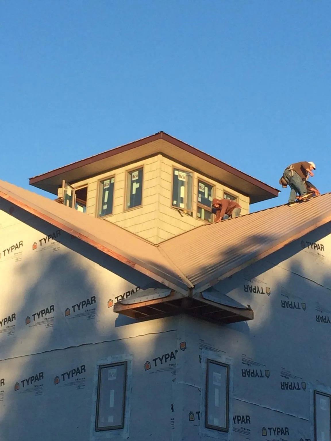 Roofers working around a rooftop cupola on a new metal roof at sunset — Roof Waterproofing in Dix by Roofing Brothers
